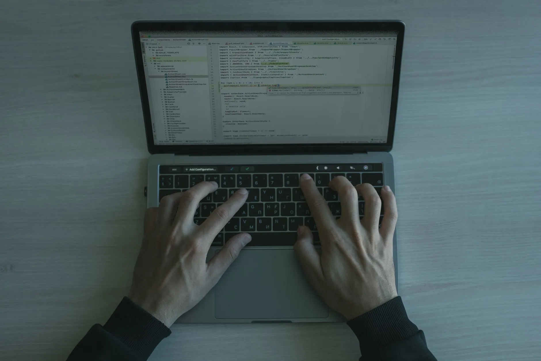 Hands on a laptop keyboard with code open on the screen, seen from above