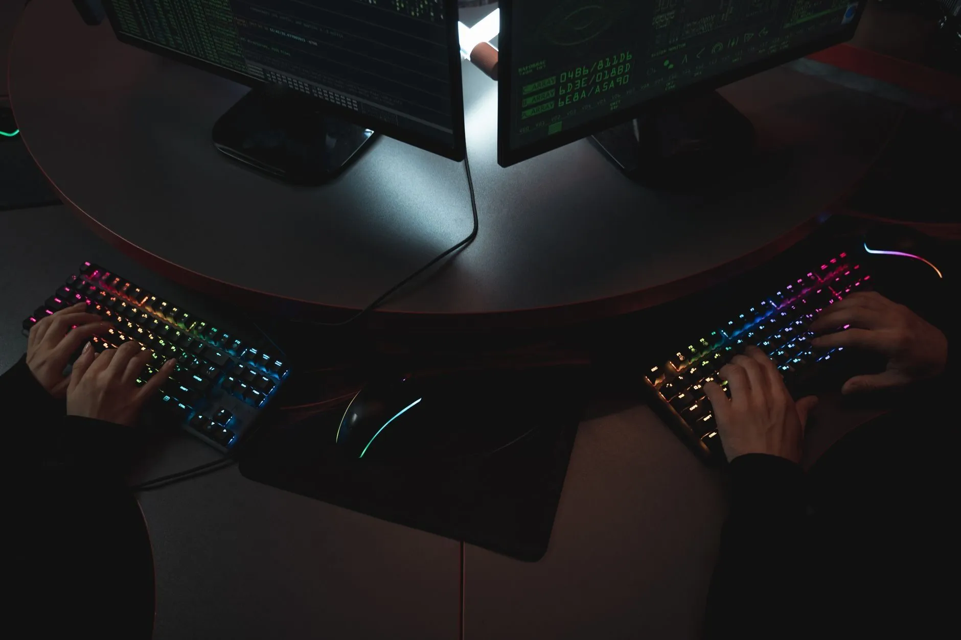 Two people typing on backlit keyboards, seen from above