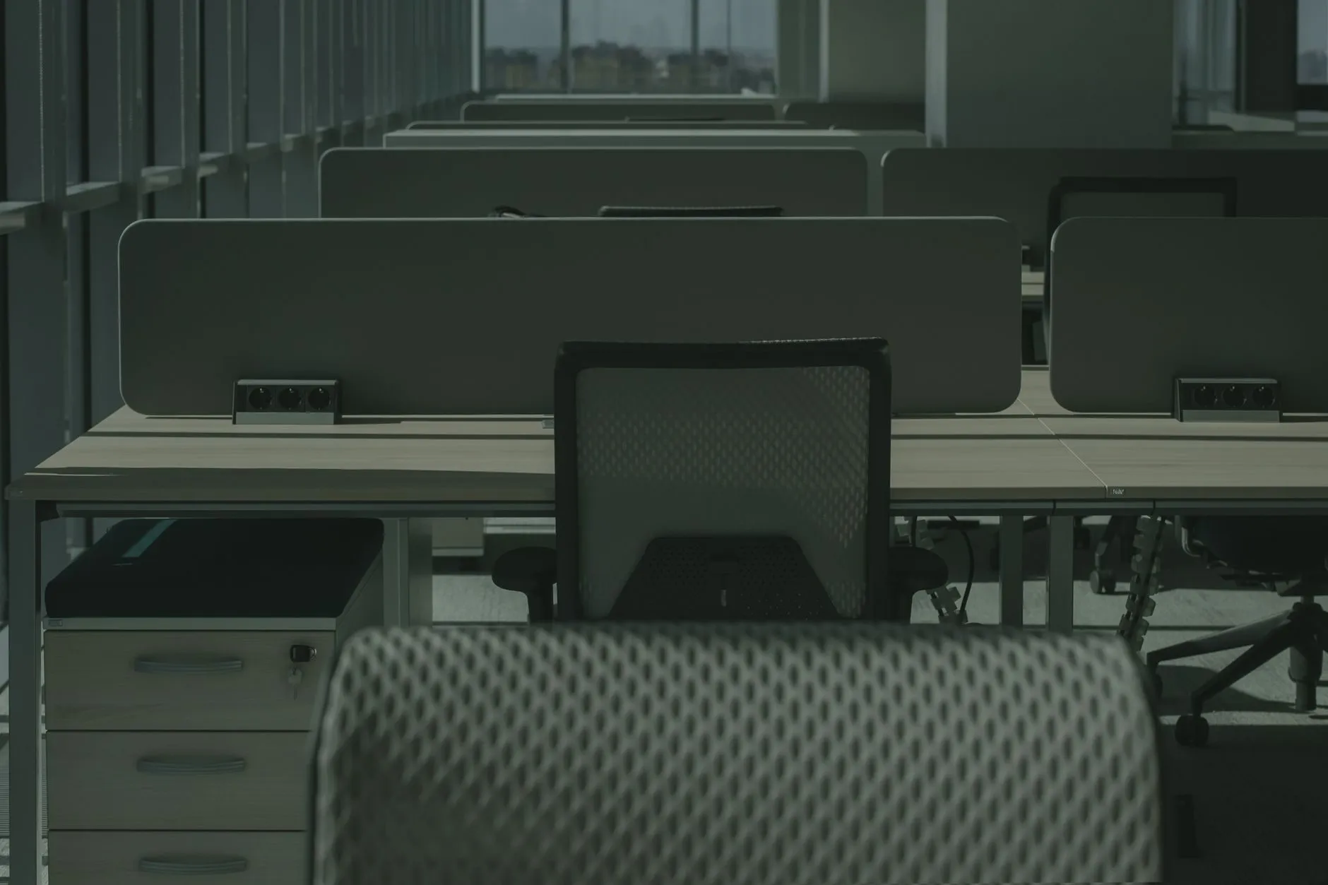 An empty open-plan office in the evening, rows of desks with a mesh chair in front